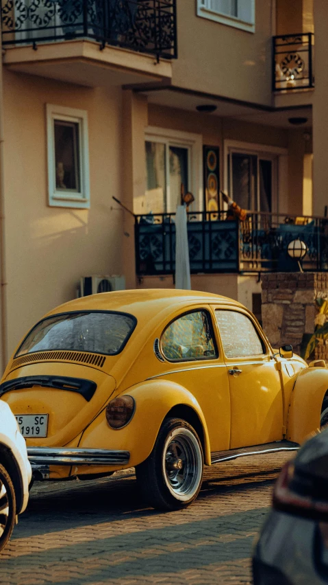 a yellow beetle sits on the street beside a building