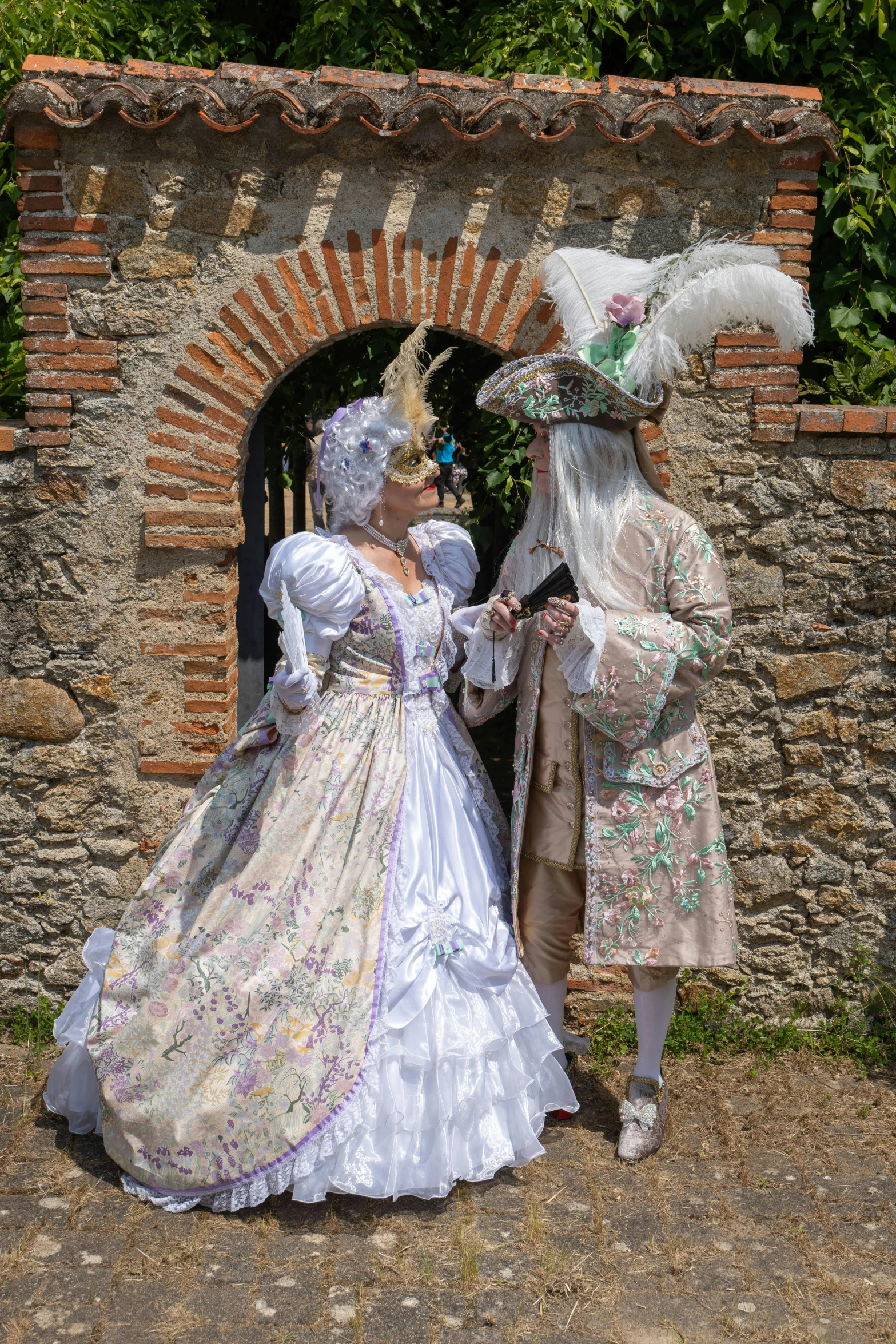 people dressed in historical costumes standing beside a brick wall