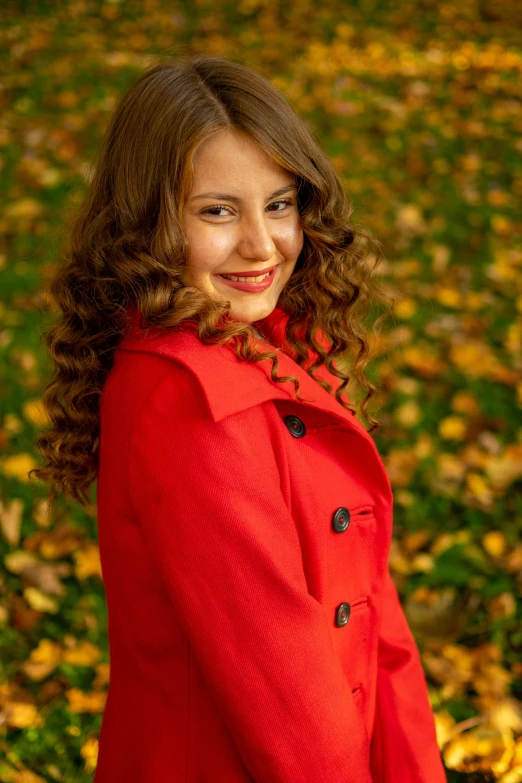 a smiling girl in a red jacket is standing in the grass