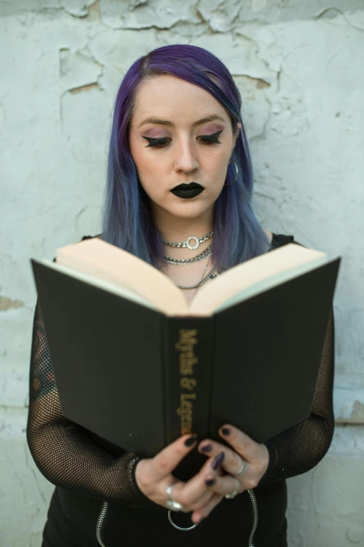 woman with blue hair wearing black makeup holding a book