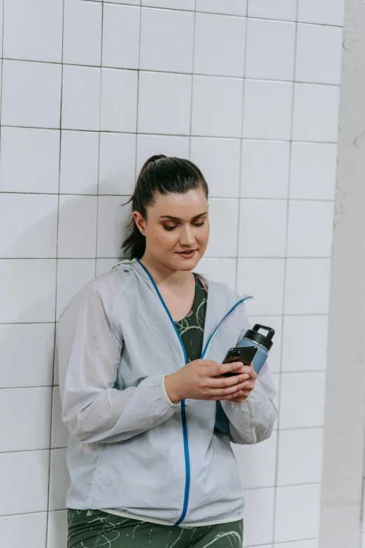 a woman texting and leaning against a wall with a cell phone