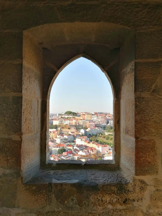 a window in an old stone building reveals a city seen through it