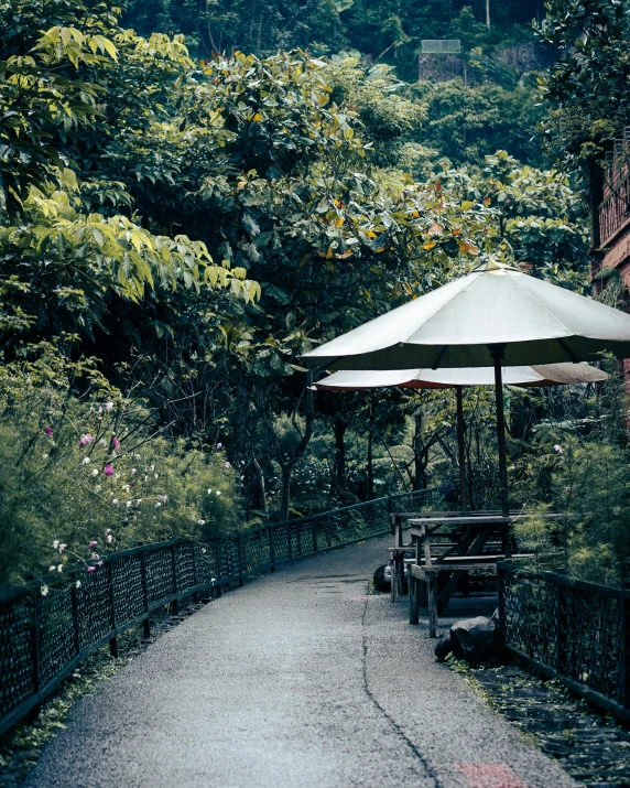 a paved path with two tables covered by an umbrella