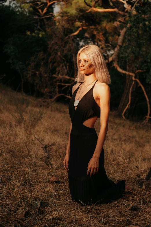 a beautiful blond woman in a black dress standing in the grass