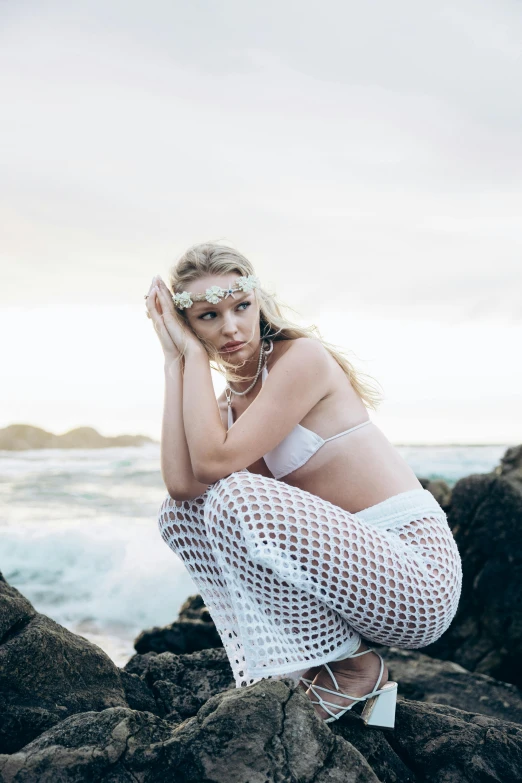 a woman with fishnet clothing posing on rocks by the sea