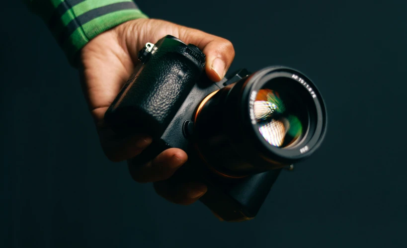 man's hand holding camera with reflection on dark background