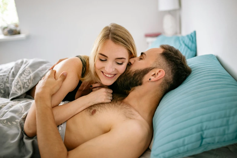 a young man laying on top of a women lying in bed