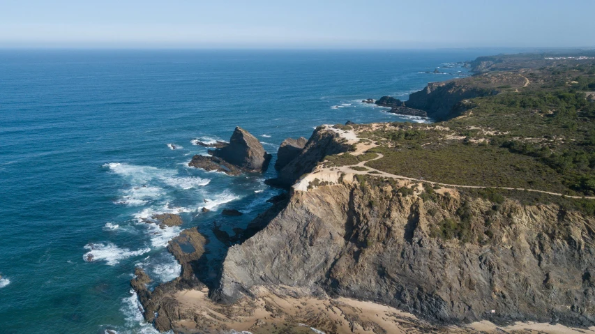 the view shows a cliff, with a road along it, near a beach area