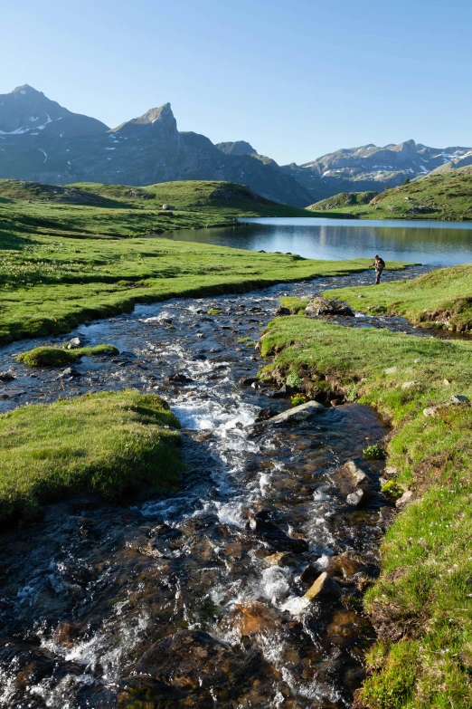 a stream near some mountains with green grass