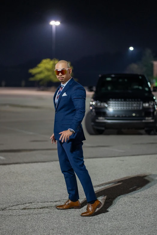 the man is standing near a car and another vehicle at night