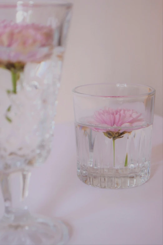 two vases and two clear cups have pink flowers
