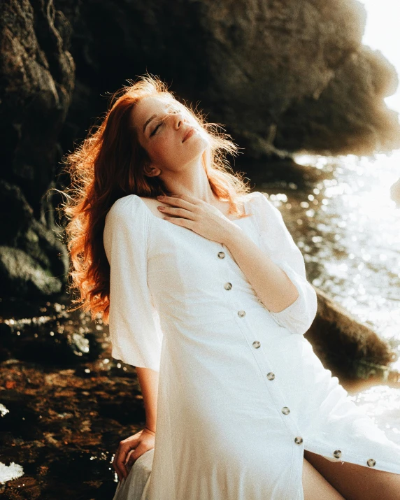 woman in white dress laying on the rocks near water