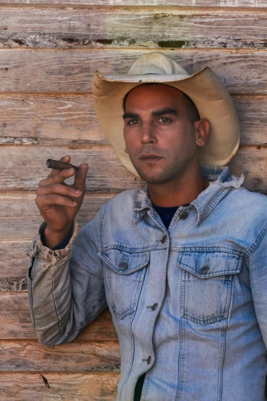 a man with cowboy hat holding up a cigarette