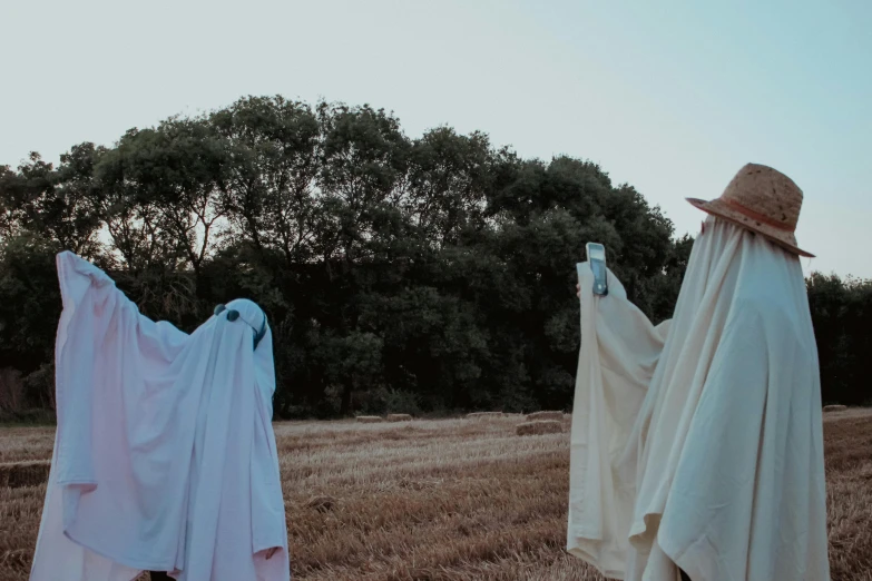 two white scarecrows with heads covered by blanket blowing in the wind