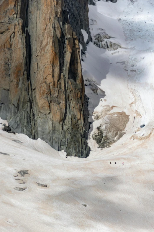 a person standing on top of a snow covered slope near a big rocky cliff