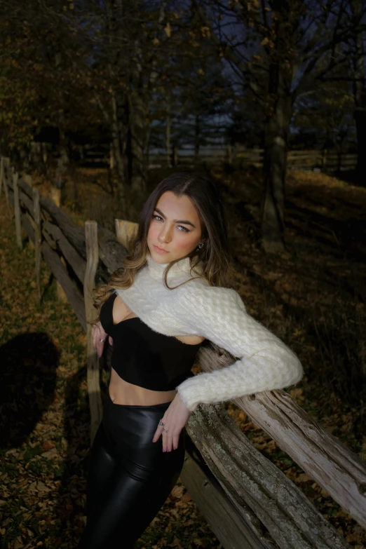 a beautiful young lady leaning on a wooden fence