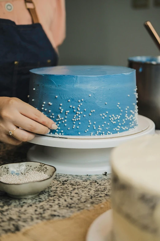 a person putting some sugar on the top of a blue cake