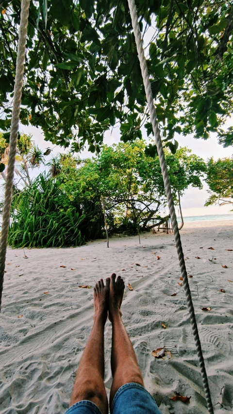 person laying on a hammock swing looking down at the beach