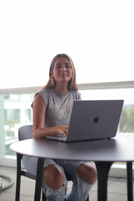 a girl is smiling as she sits at a table with her laptop in front of her