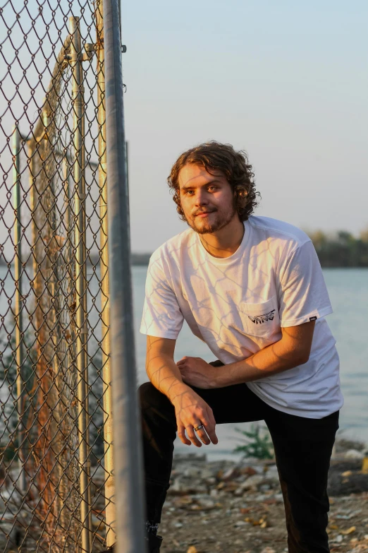 a man sitting in front of a fence near the water