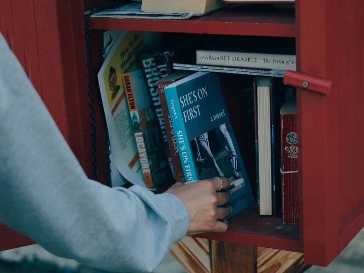 a person touching books on top of a red shelf