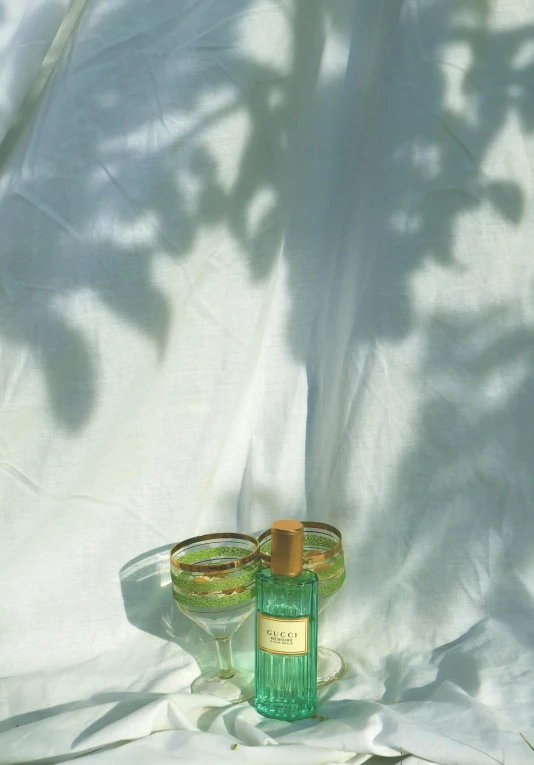 a green bottle and glass sit on a white sheet