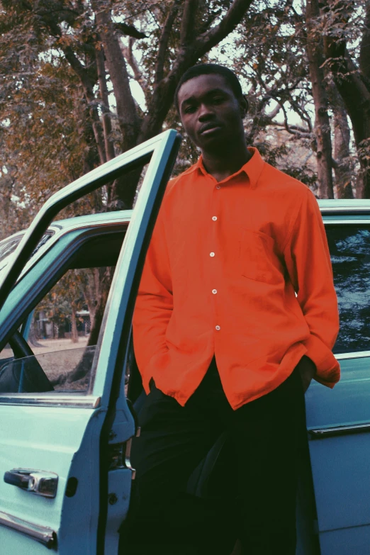 man in orange shirt leaning against a parked car