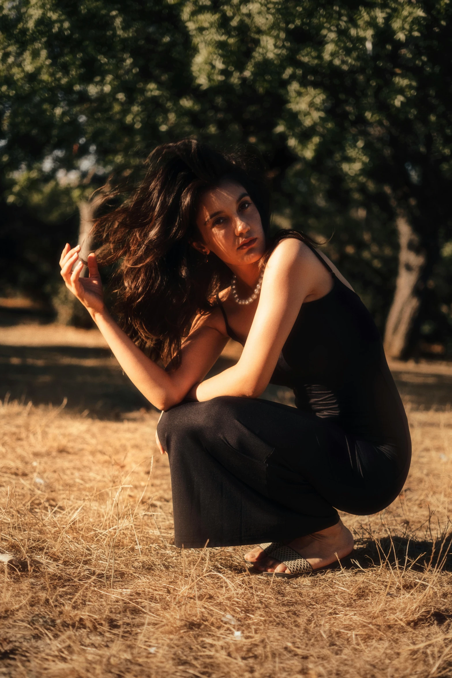 a young woman crouches in the grass next to trees