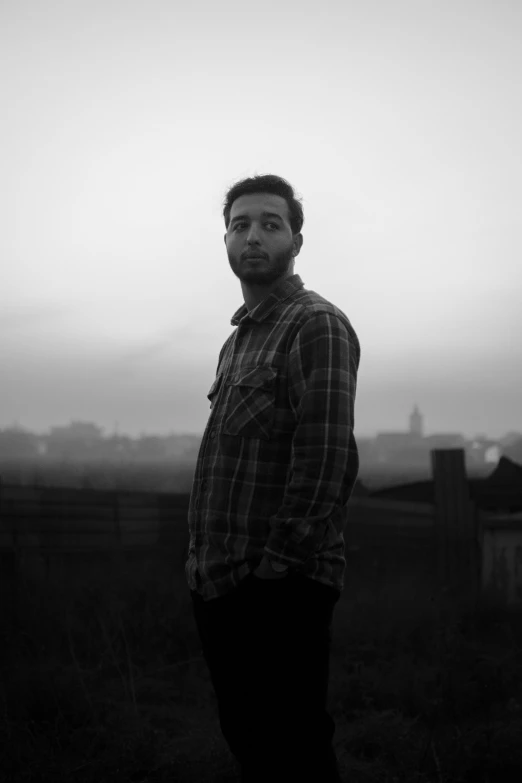 a person stands in a field wearing a plaid shirt