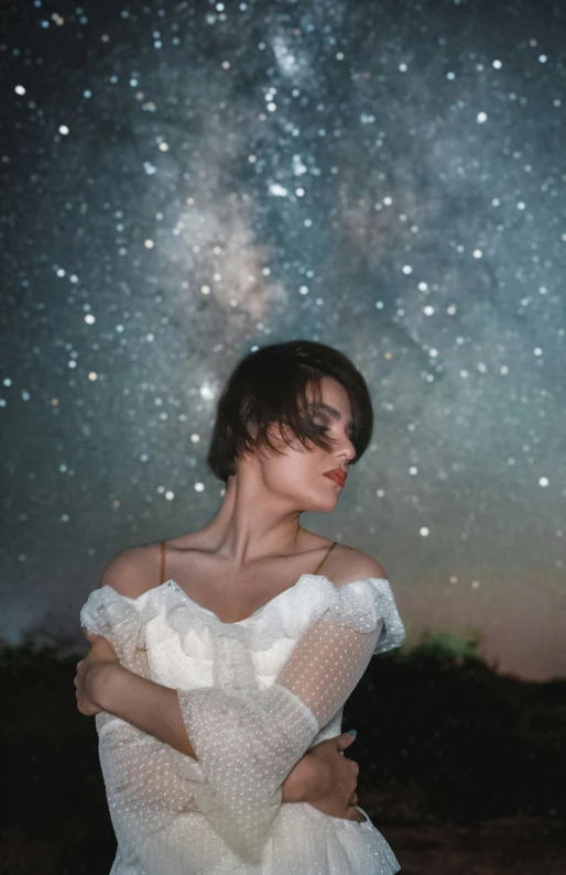 a woman wearing a white dress and glasses standing on a hillside under the stars of the night sky