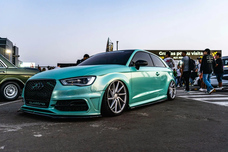 a blue audi at an auto show with cars and people walking in front