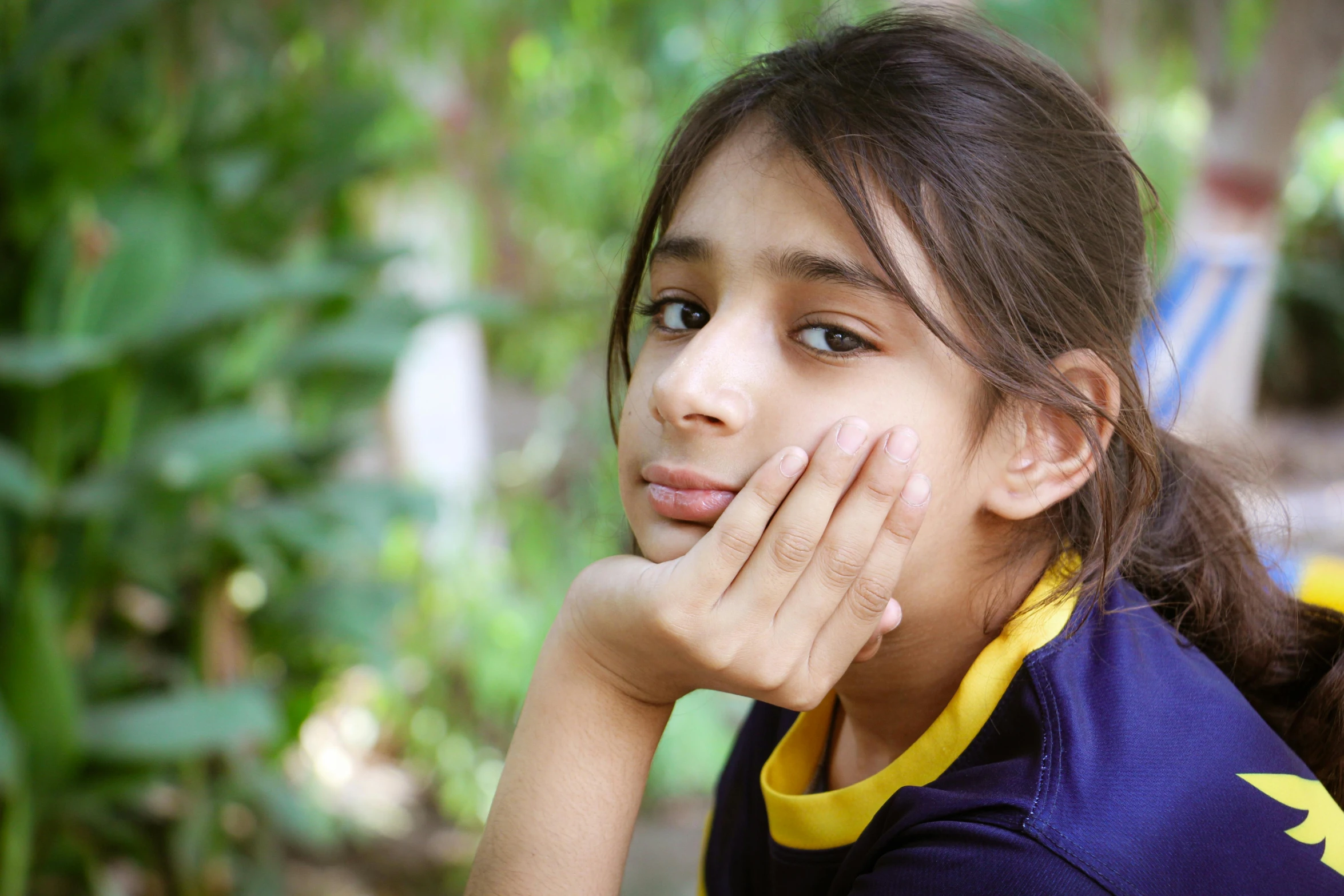 girl with hand to her face sitting next to some plants