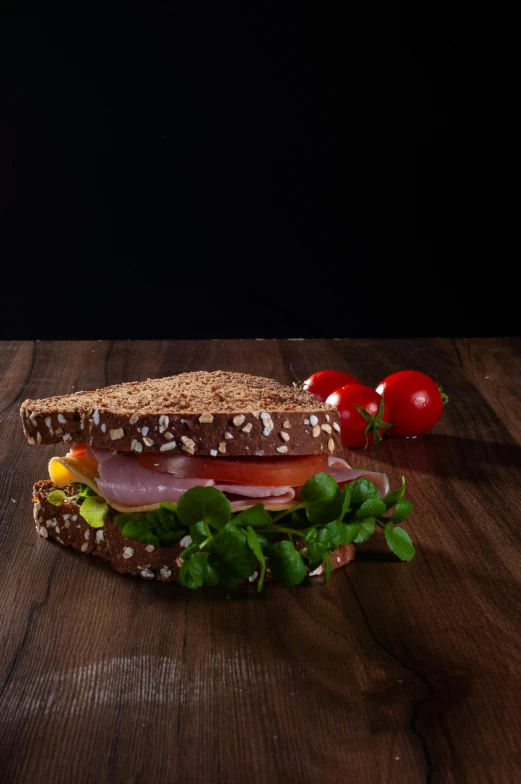 sandwich displayed on wooden table with tomatoes, lettuce and tomato