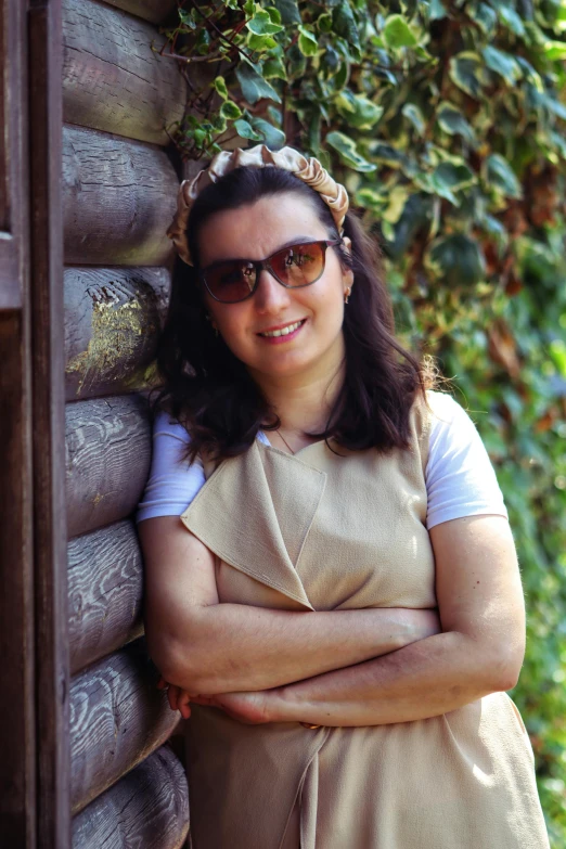 a smiling woman leaning on the side of a building with her arms crossed