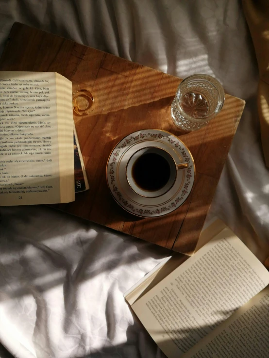 an open book and a cup sitting on top of a wooden tray