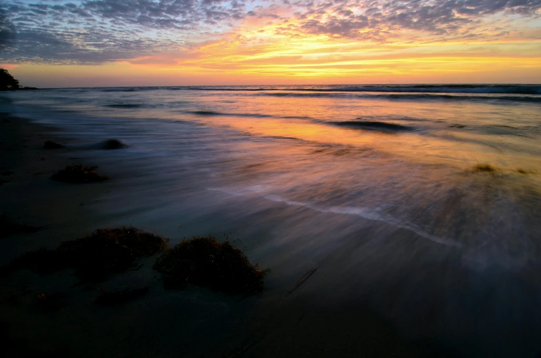 a sunset on the beach with waves crashing up against the shoreline