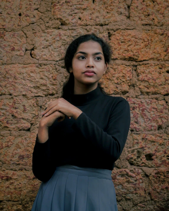 a girl leaning against a rock wall and looking down at the camera