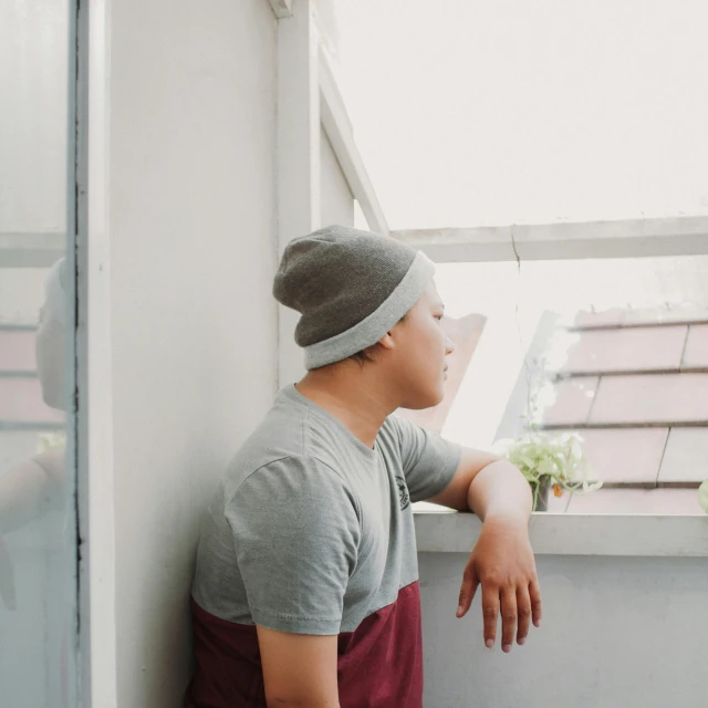 a young man standing near a window with his hands on the window sill