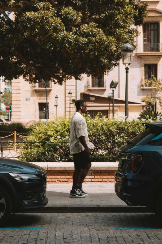 a man stands near two cars on a city street