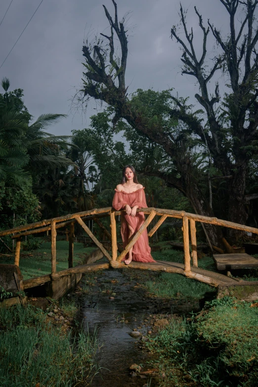 a woman wearing a pink dress standing on a bridge