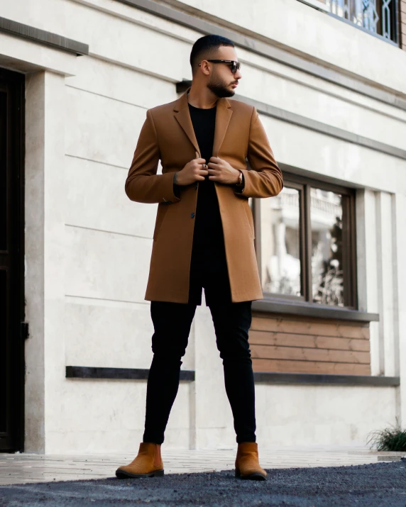 man in camel coat and brown boots with a black outfit and tan shoes