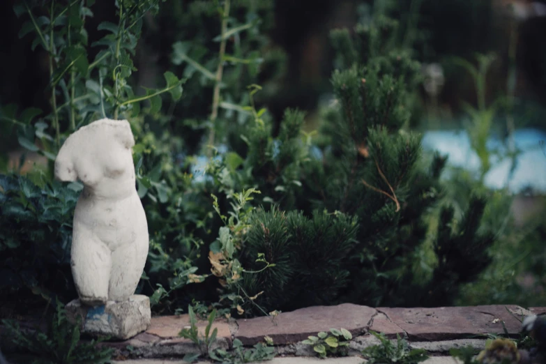 there is a statue sitting next to some shrubbery