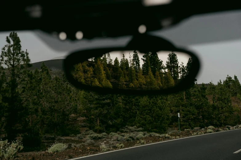 a rear view mirror with trees and hills in the back