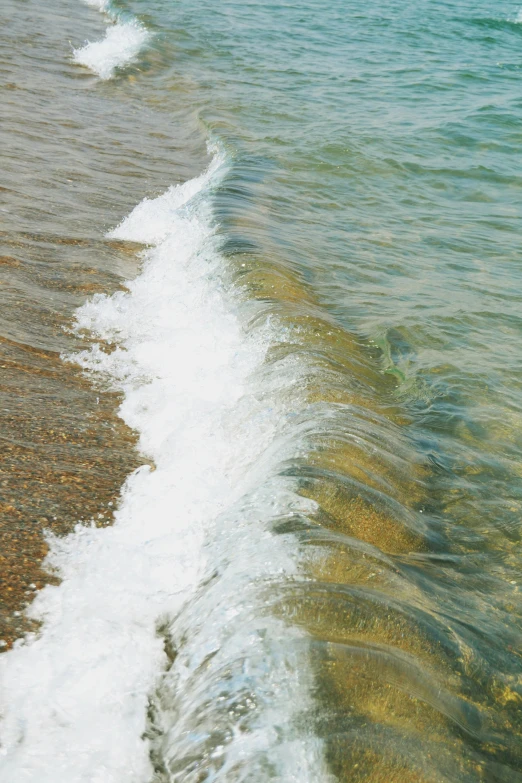 a wave comes up to the beach with white foam on top