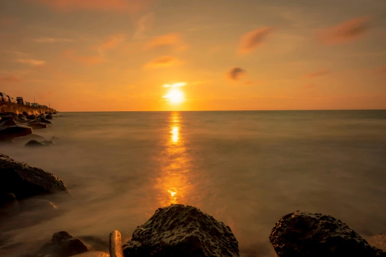 the sun rising behind the horizon, on a beach with rock formations