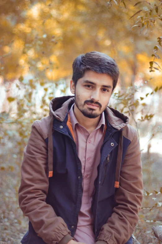 man with beard sitting down in the middle of a wooded area