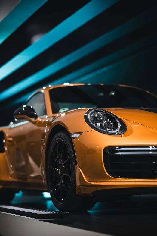 an orange sports car on display in front of a blue and green background