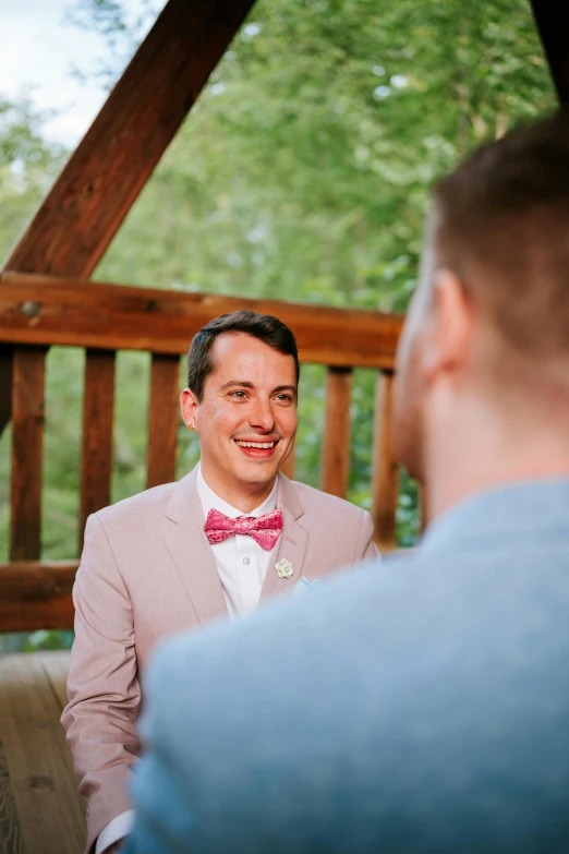 a man in a pink jacket and bow tie is talking to another person