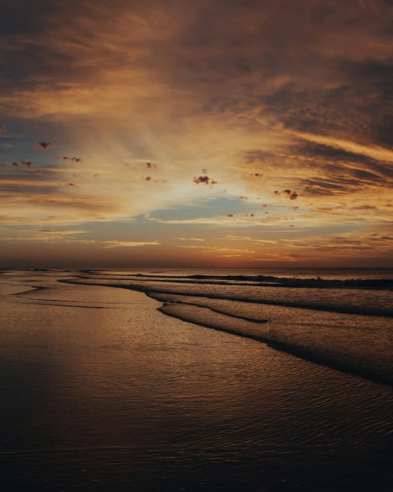 people are sitting at the edge of the beach as the sun sets