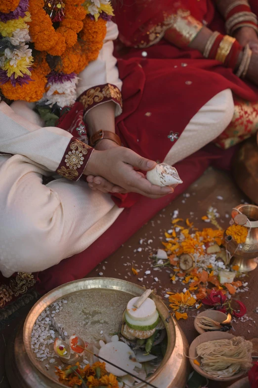 indian bride dressed in traditional red holding small plate with food and flowers